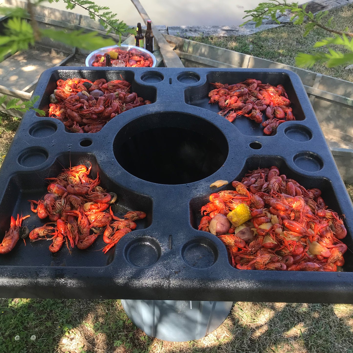 Black plastic seafood table filled with crawfish over a garage can outside